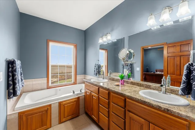 a bathroom with a granite countertop sink a large mirror and a bathtub next to a window