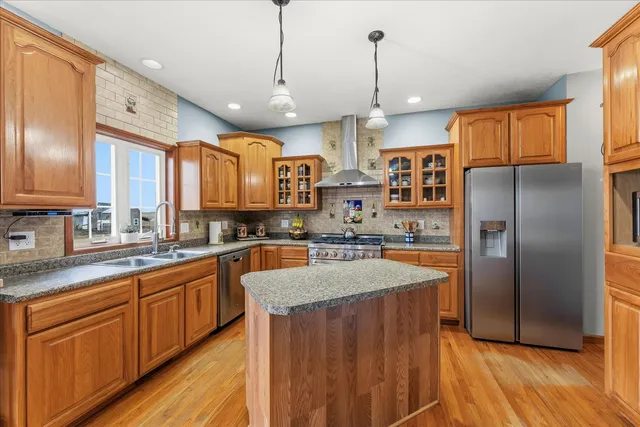 a large kitchen with stainless steel appliances kitchen island granite countertop a refrigerator a sink dishwasher a stove and white cabinets with wooden floor