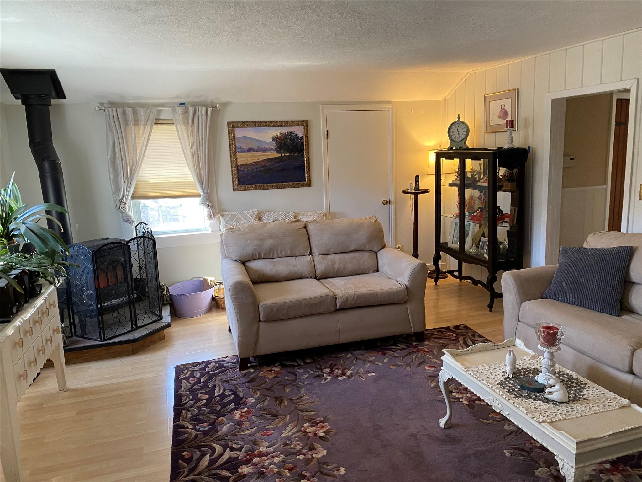 168 Prospect Road Monroe, NY 10950 - Photo 3 of 15 Living room featuring wooden walls, a textured ceiling, a wood stove, and light wood finished floors