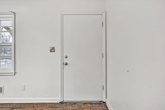 a view of an empty room with wooden floor and a window