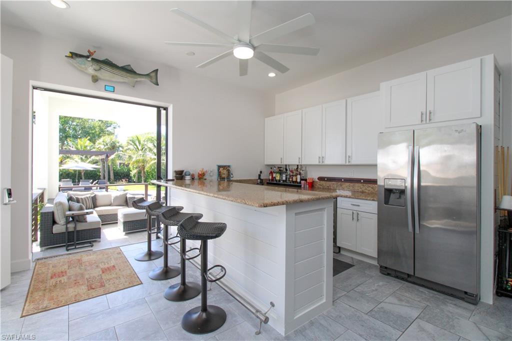 1555 Crayton Road Naples, FL 34102 - Photo 29 of 50 Kitchen with stone counters, stainless steel fridge with ice dispenser, kitchen peninsula, a breakfast bar, and white cabinets