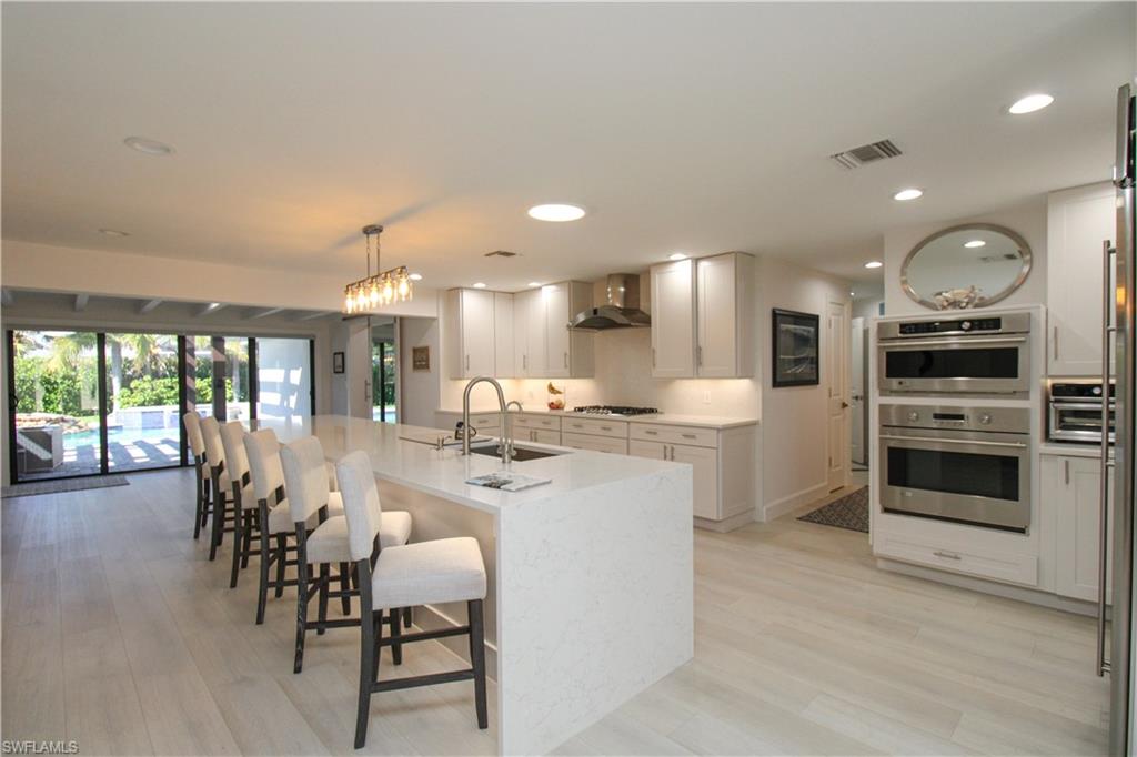 1555 Crayton Road Naples, FL 34102 - Photo 7 of 50 Kitchen with sink, wall chimney range hood, gas cooktop, decorative light fixtures, and a kitchen island with sink
