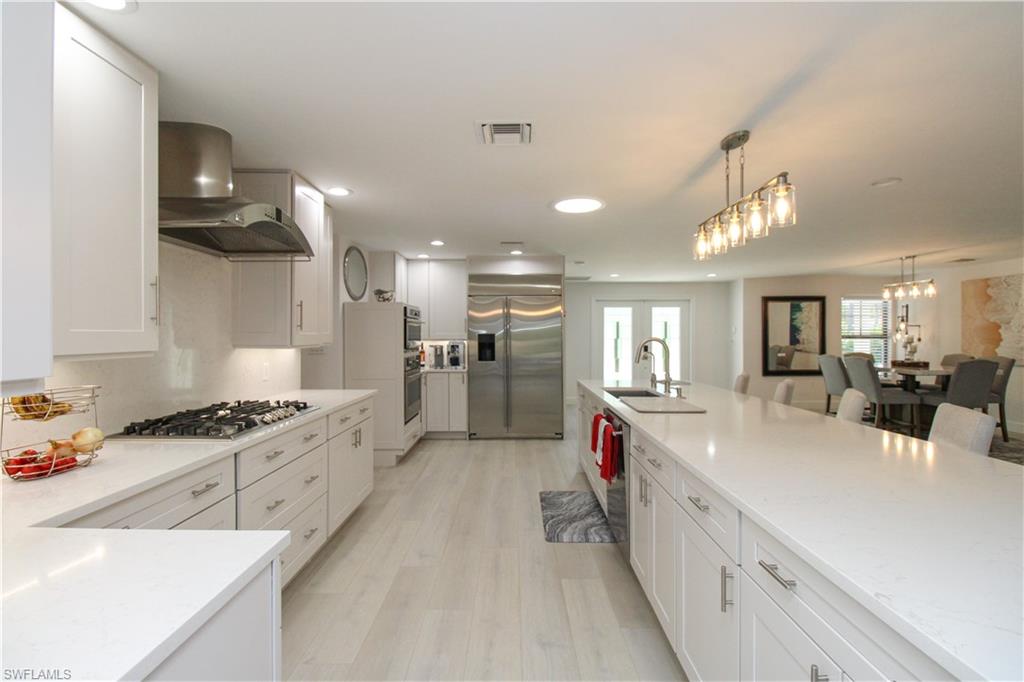 1555 Crayton Road Naples, FL 34102 - Photo 10 of 50 Kitchen featuring wall chimney exhaust hood, hanging light fixtures, appliances with stainless steel finishes, white cabinets, and light wood-type flooring
