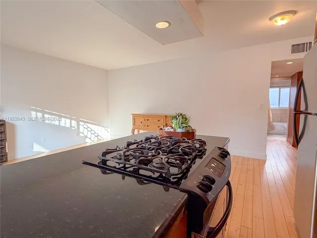 a view of a refrigerator in kitchen and an empty room with wooden floor