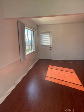 an empty room with wooden floor and windows with curtains