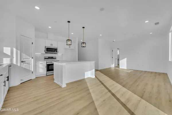 a large white kitchen with kitchen island a refrigerator a stove a sink dishwasher and white cabinets with wooden floor