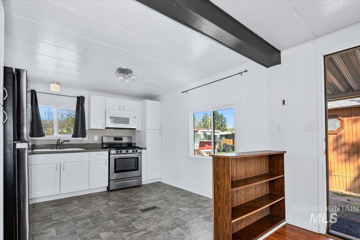 7701 West Ustick Road, Unit 14 Boise, ID 83704 - Photo 8 of 22 Kitchen with white cabinetry, gas stove, freestanding refrigerator, dark countertops, and wooden walls