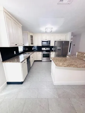 a large kitchen with kitchen island granite countertop a sink a stove top oven and white cabinets