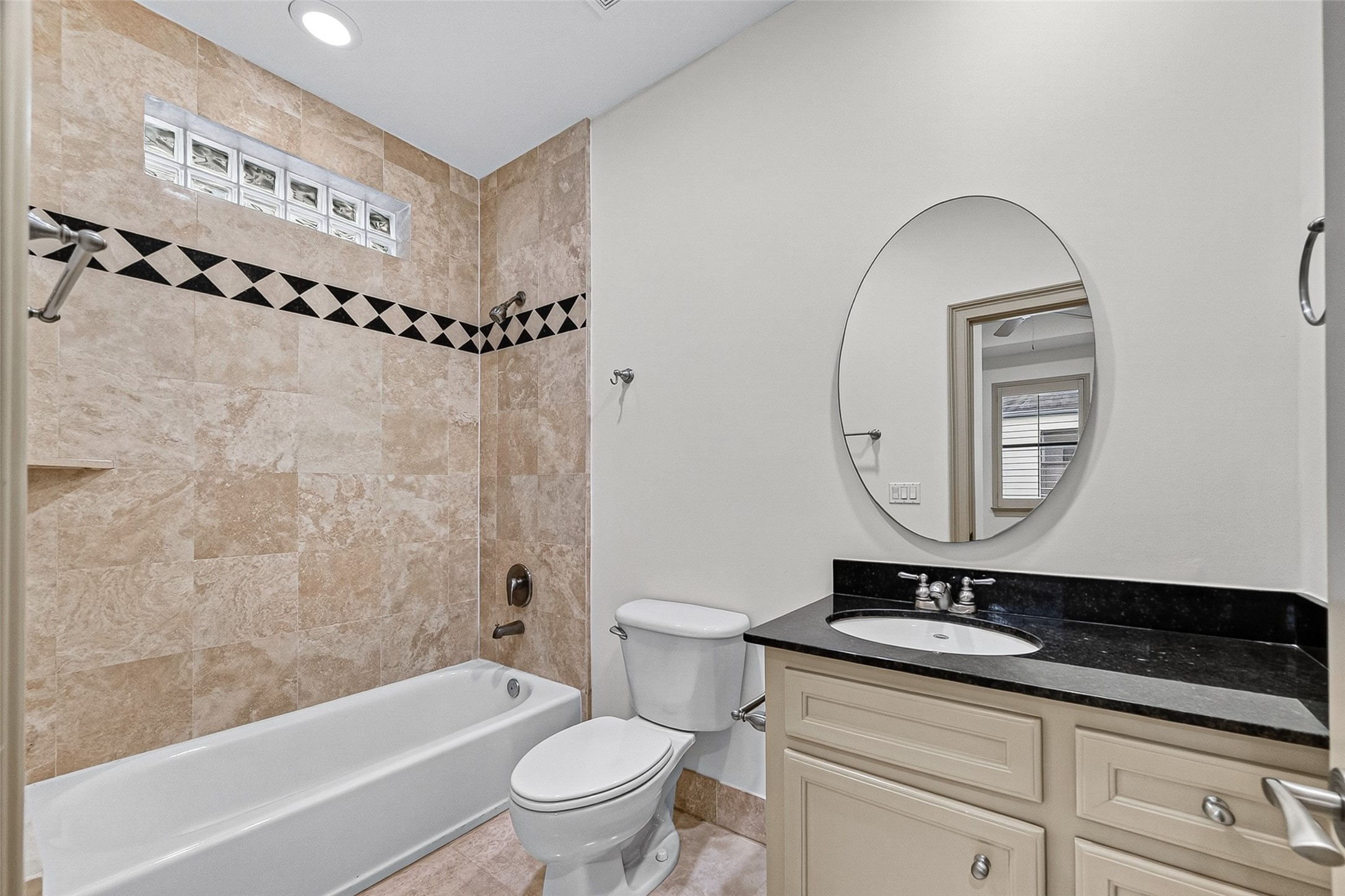 2034 Colquitt Street, Unit A Houston, TX 77098 - Photo 35 of 41 This 3rd floor ensuite bathroom features elegant beige tilework with a decorative border, a combination shower and tub, and a sleek vanity with a black countertop and oval mirror.