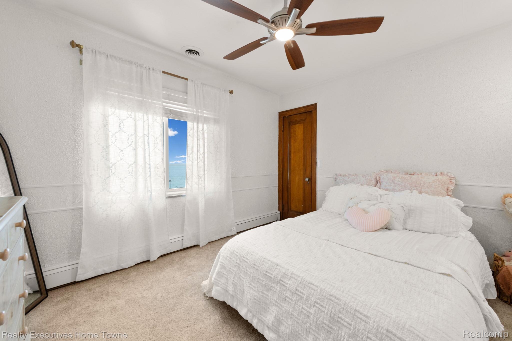 8308 Lakeshore Road Fort Gratiot, MI 48059 - Photo 56 of 79 Bedroom featuring wainscoting, an overhead ceiling fan with lighting, a window with a valance and white drapes, and a wood-finish door