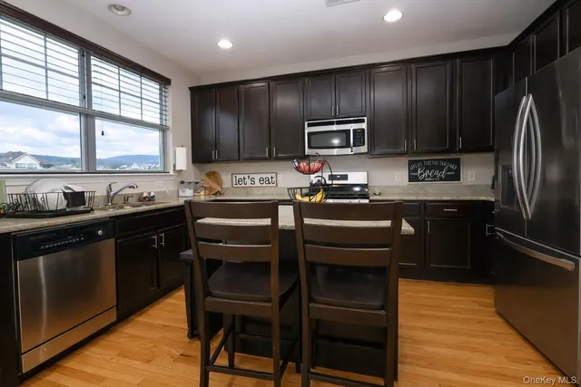 a kitchen with stainless steel appliances granite countertop wooden cabinets a refrigerator a stove a sink and dishwasher with wooden floor