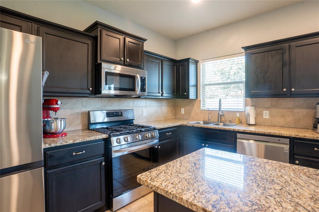 753 Rutherford Drive Crowley, TX 76036 - Photo 9 of 26 Kitchen featuring dark wood cabinetry, granite countertops, tile backsplash, and stainless steel appliances including a gas range and built-in microwave