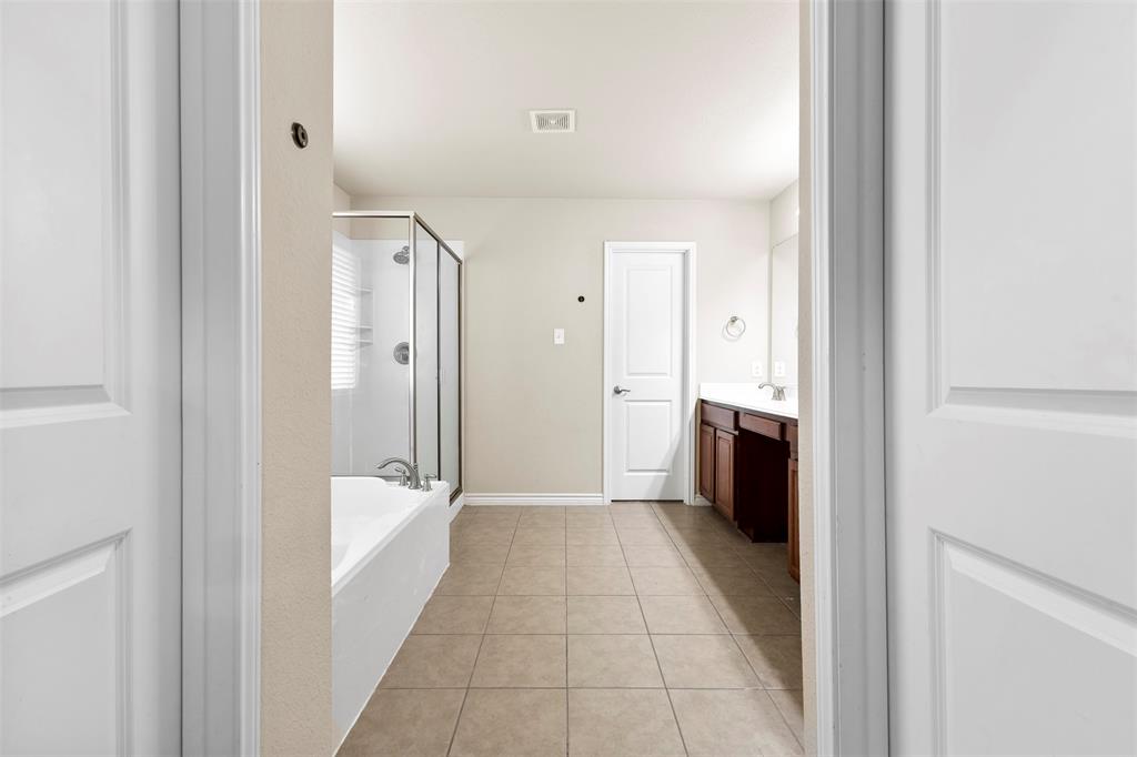 6522 Portside Ridge Lane Dallas, TX 75249 - Photo 15 of 37 Spacious bathroom featuring neutral tile flooring, a built-in tub with a glass shower enclosure, and a double vanity with dark wood cabinetry