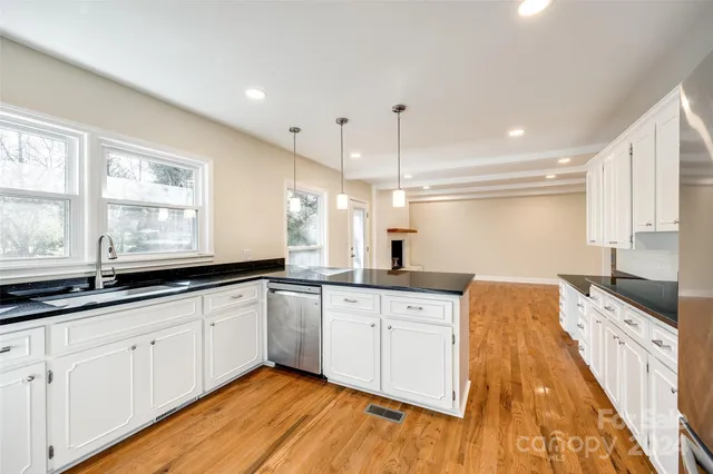 a large kitchen with granite countertop a sink and white cabinets with wooden floor