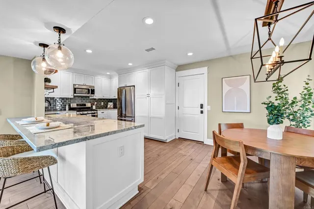 a kitchen with stainless steel appliances kitchen island granite countertop a refrigerator a stove top oven a dining table and chairs with wooden floor