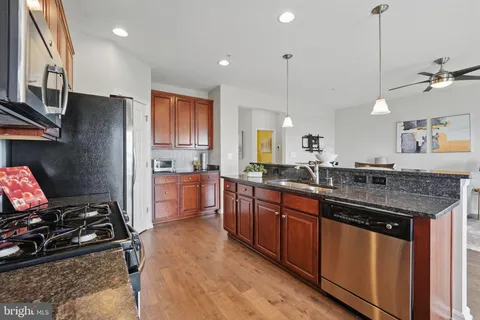 a kitchen with stainless steel appliances granite countertop a stove a sink dishwasher a refrigerator and a wooden cabinets with wooden floor