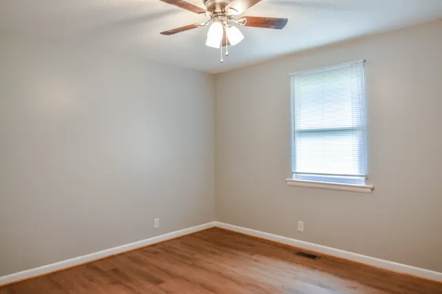 an empty room with wooden floor chandelier fan and windows
