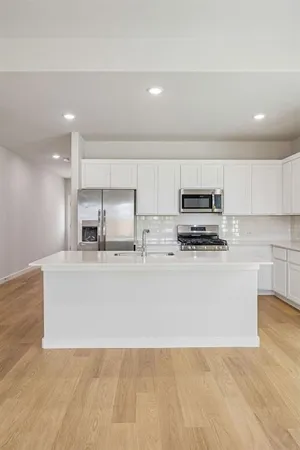 a view of kitchen with stainless steel appliances granite countertop a stove a sink a refrigerator and white cabinets with wooden floor