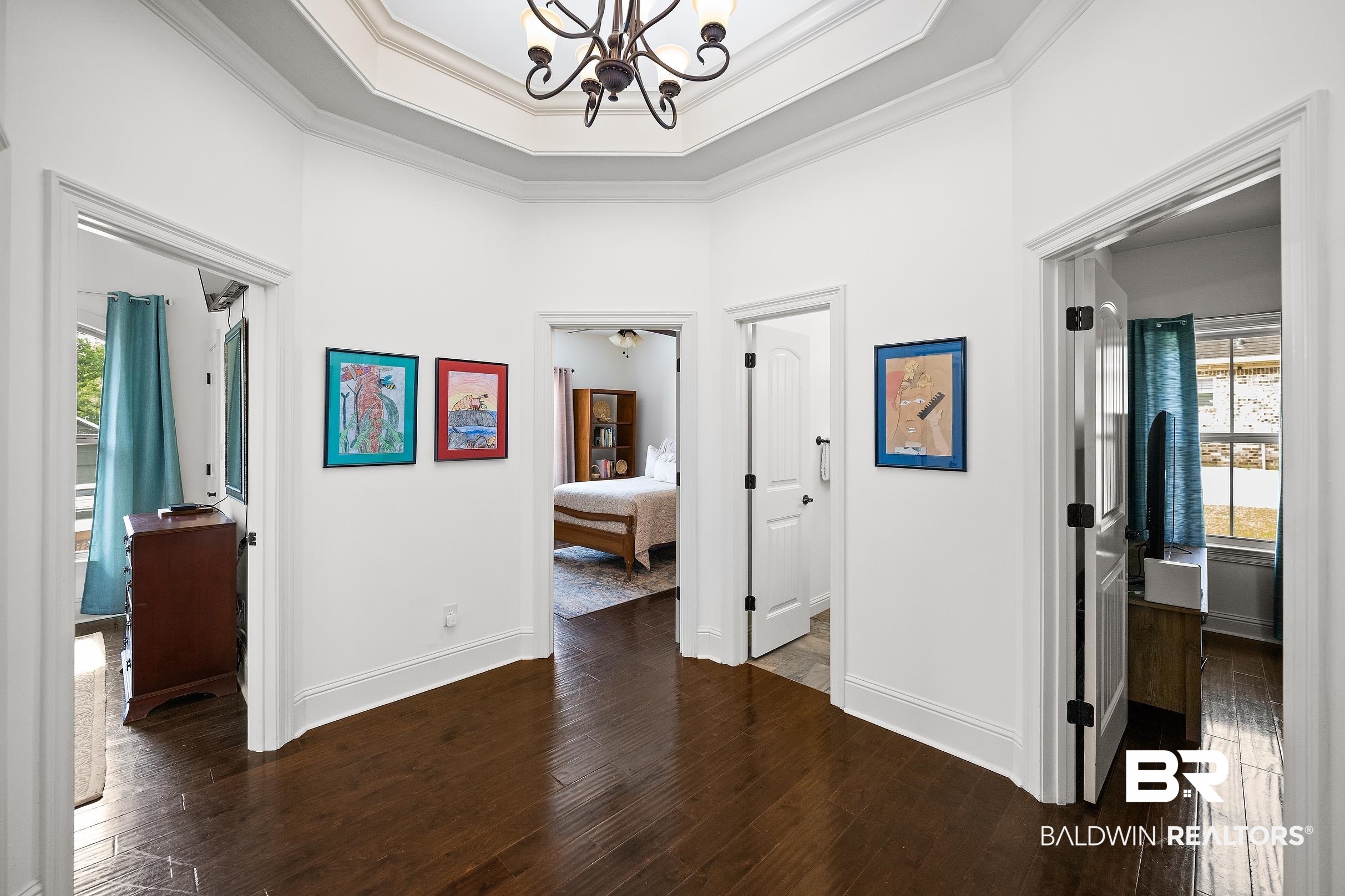 313 Pecan Ridge Boulevard Fairhope, AL 36532 - Photo 16 of 51 Central hallway featuring dark wood-finish flooring, white walls, and a tray ceiling with a chandelier