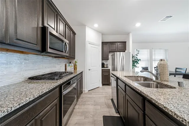 a kitchen with granite countertop stainless steel appliances a sink dishwasher a stove top oven a refrigerator with wooden cabinets and floor