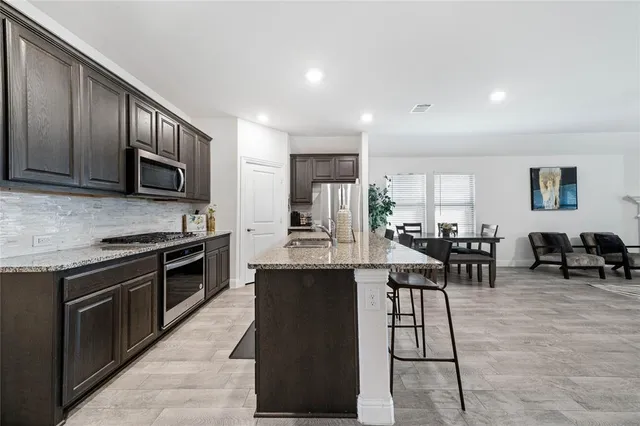 a kitchen with stainless steel appliances kitchen island granite countertop a stove a sink a dining table and chairs