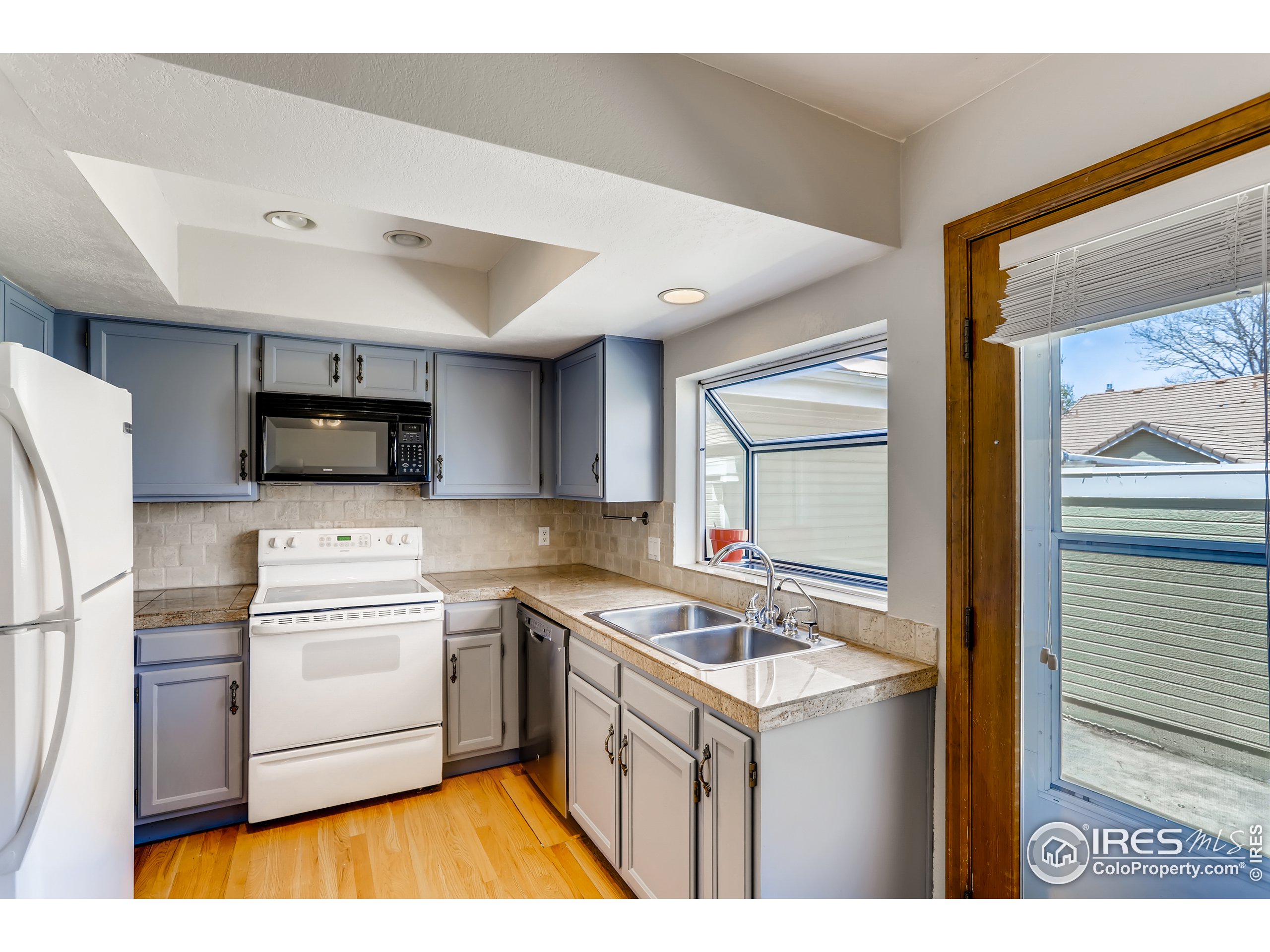 2315 Ranch Drive Westminster, CO 80234 - Photo 6 of 28 a kitchen that has a sink a stove top oven a refrigerator and white cabinets with wooden floor