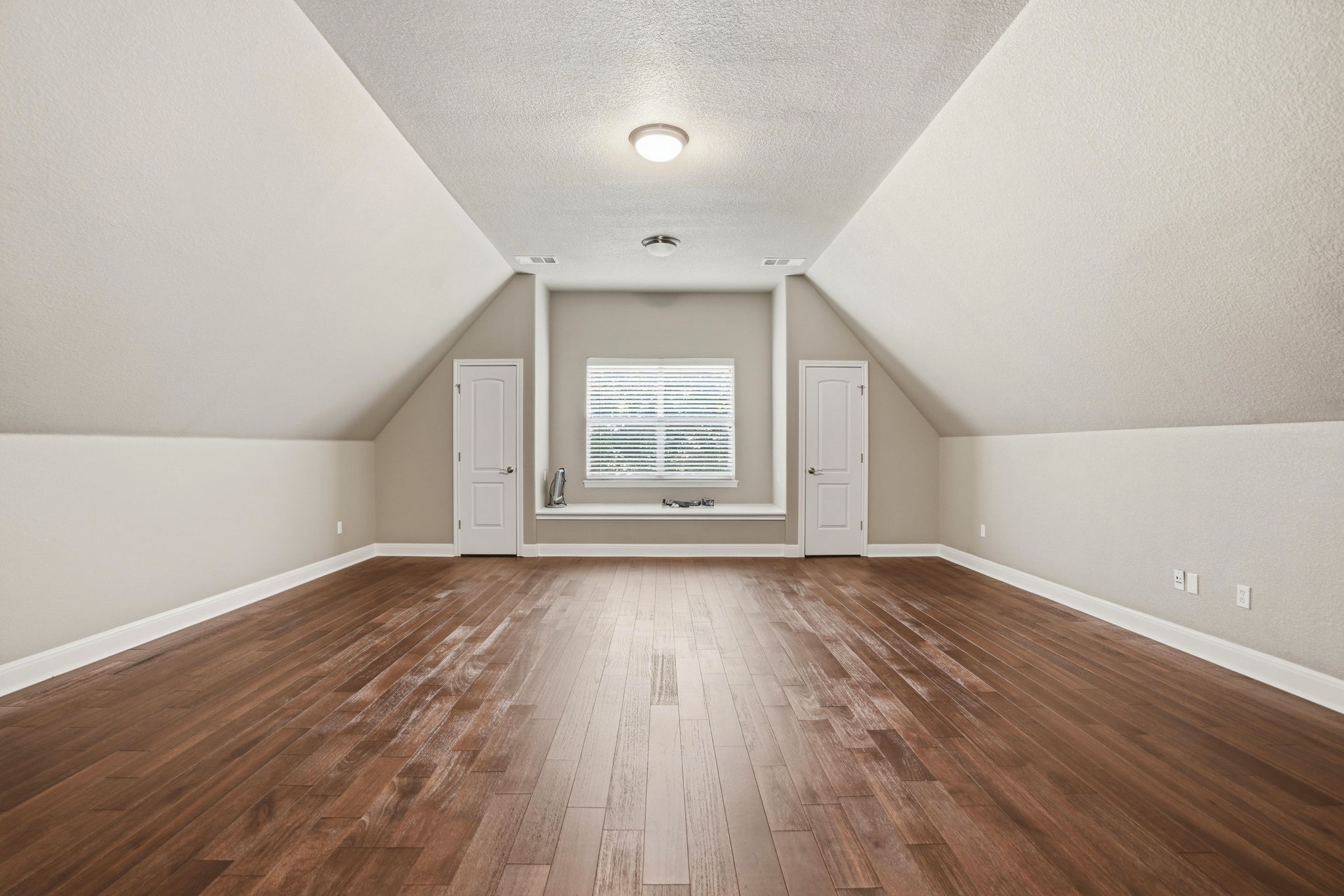 222 Vailco Lane Austin, TX 78738 - Photo 37 of 39 Spacious room featuring wood-finish flooring, neutral paint tones, sloped ceilings, a central window with blinds, and two white panel doors