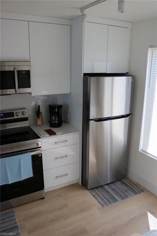 2235 San Marco Road, Unit 5204 Marco Island, FL 34145 - Photo 21 of 34 Compact kitchen featuring stainless steel appliances, white cabinetry, track lighting, light wood-finish flooring, and white countertops