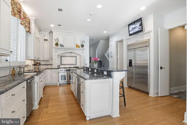 a kitchen with stainless steel appliances granite countertop a stove a sink dishwasher and white cabinets with wooden floor