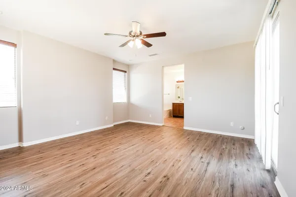 an empty room with wooden floor ceiling fan and windows