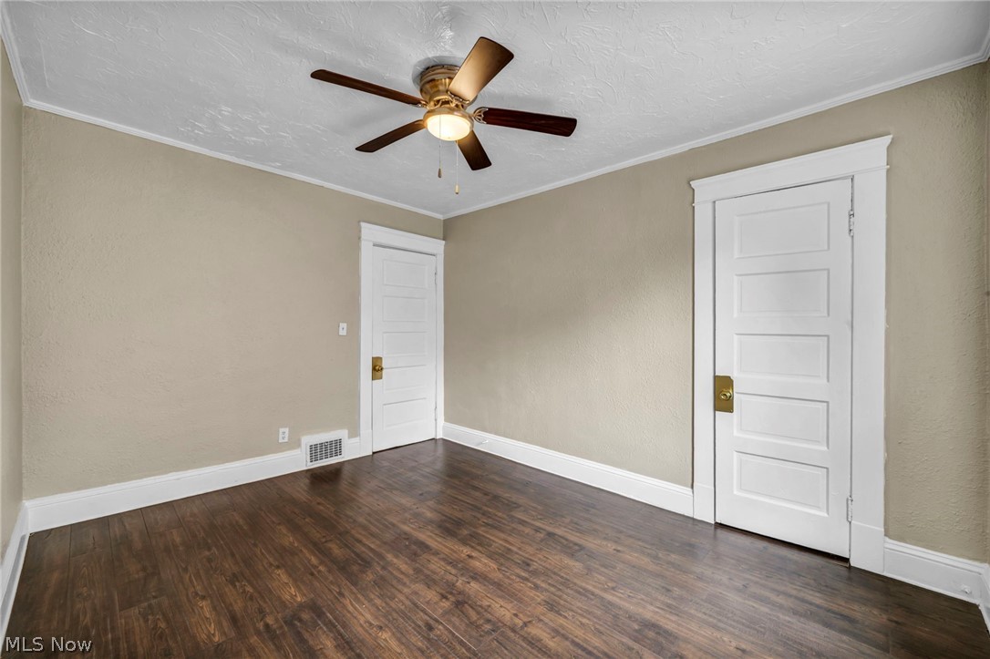 1677 Carlyon Road East Cleveland, OH 44112 - Photo 19 of 41 Spare room with ornamental molding, a textured ceiling, dark wood-style flooring, a textured wall, and a ceiling fan