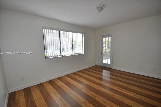 a view of an empty room with wooden floor and a window