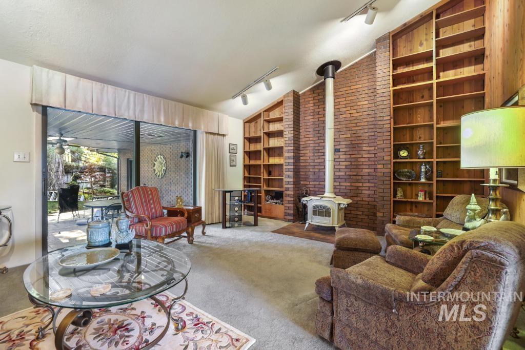 2018 Rancho Vista Drive Twin Falls, ID 83301 - Photo 19 of 50 Vaulted ceiling living area featuring a brick accent wall, a freestanding wood-burning stove, and two built-in wood shelving units