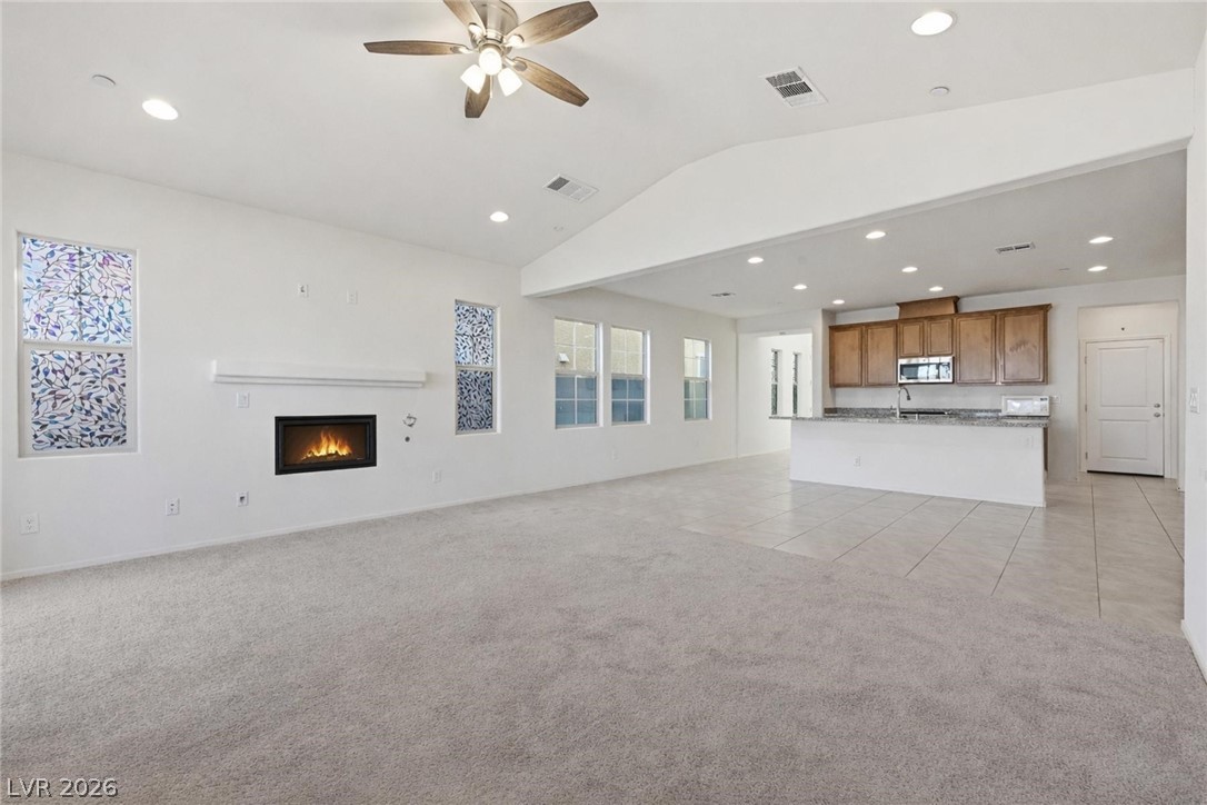 250 Dedication Avenue Henderson, NV 89011 - Photo 10 of 67 Unfurnished living room featuring a glass covered fireplace, light colored carpet, vaulted ceiling, ceiling fan, and recessed lighting