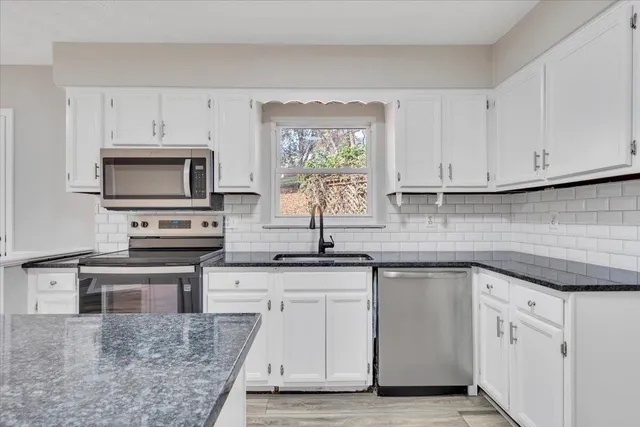 a kitchen with granite countertop a sink stainless steel appliances and white cabinets