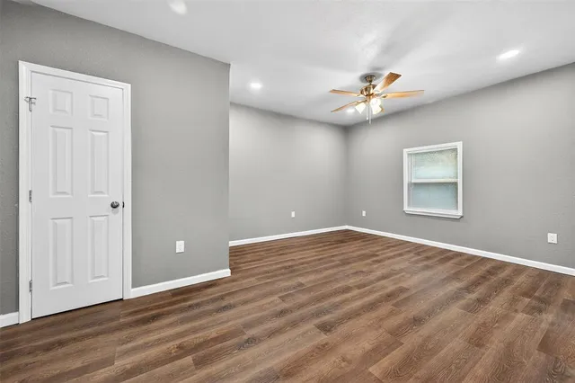 an empty room with wooden floor chandelier fan and windows