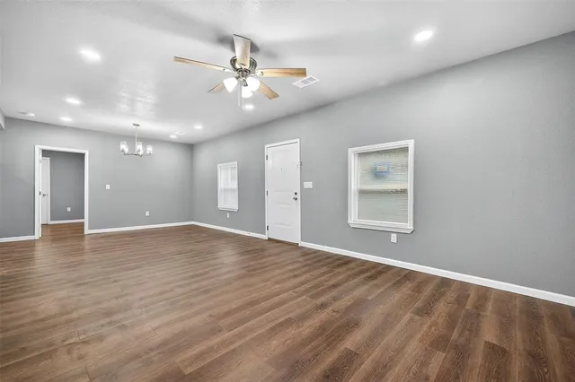 an empty room with wooden floor chandelier and windows