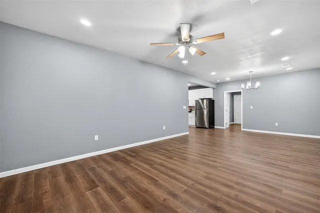 a view of an empty room with wooden floor and a ceiling fan