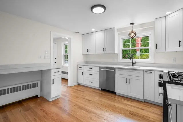 a kitchen with stainless steel appliances a sink cabinets wooden floor and a window