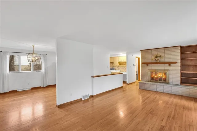 an empty room with wooden floor fire place and windows