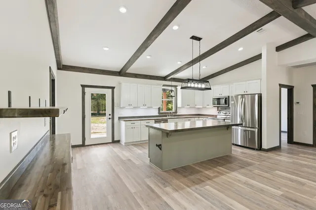 a kitchen with stainless steel appliances granite countertop a refrigerator a sink dishwasher a stove and white countertops with wooden floor