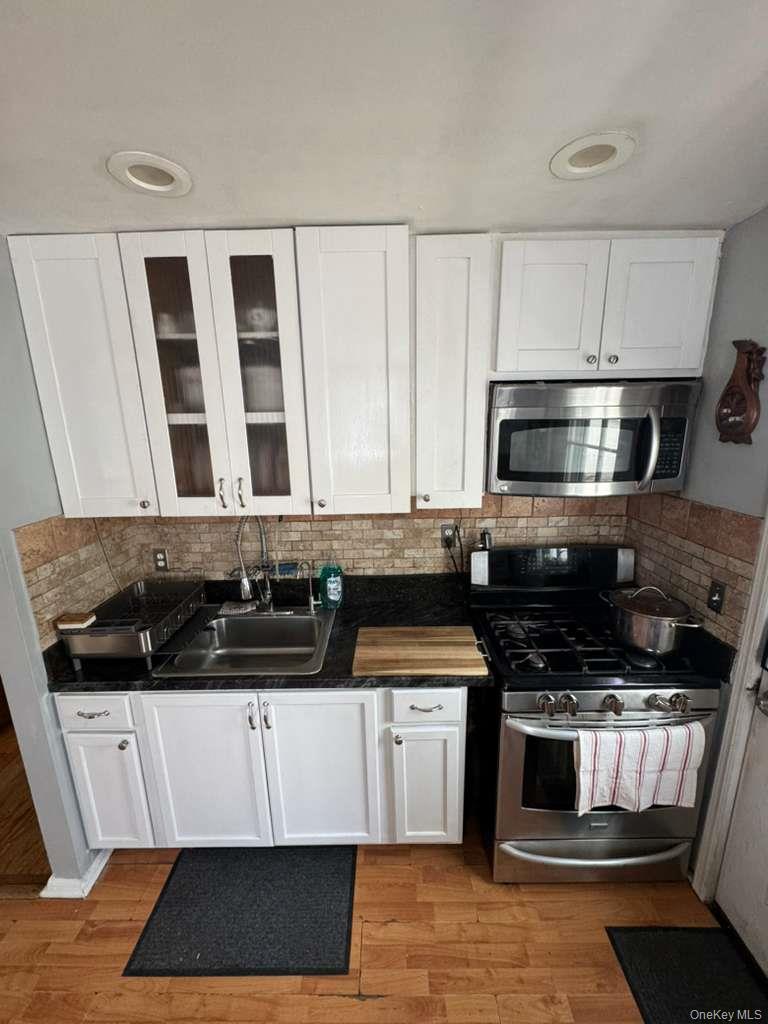 35 Harvard Street Valley Stream, NY 11580 - Photo 12 of 19 Kitchen with white cabinetry, appliances with stainless steel finishes, backsplash, glass insert cabinets, and light wood-style flooring