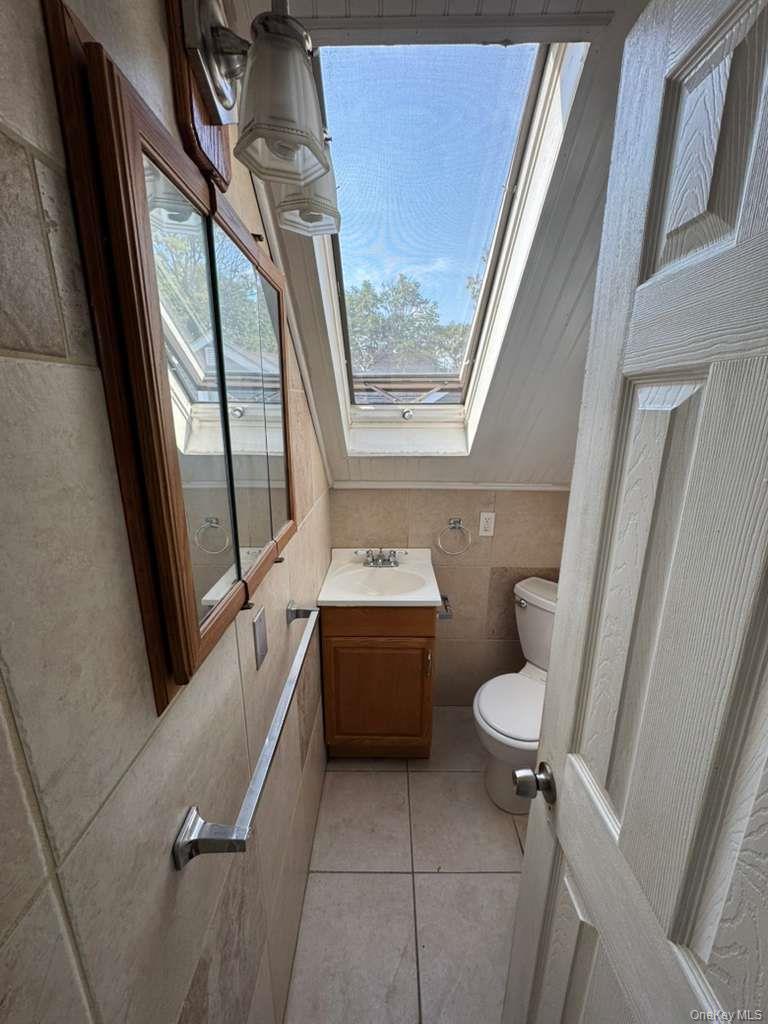 35 Harvard Street Valley Stream, NY 11580 - Photo 18 of 19 Half bath with a skylight, vanity, light tile patterned floors, and tile walls
