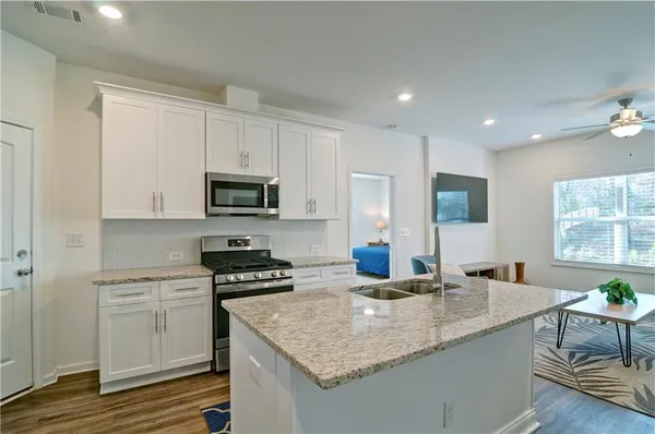 a kitchen with granite countertop stainless steel appliances sink stove microwave and white cabinets with wooden floor