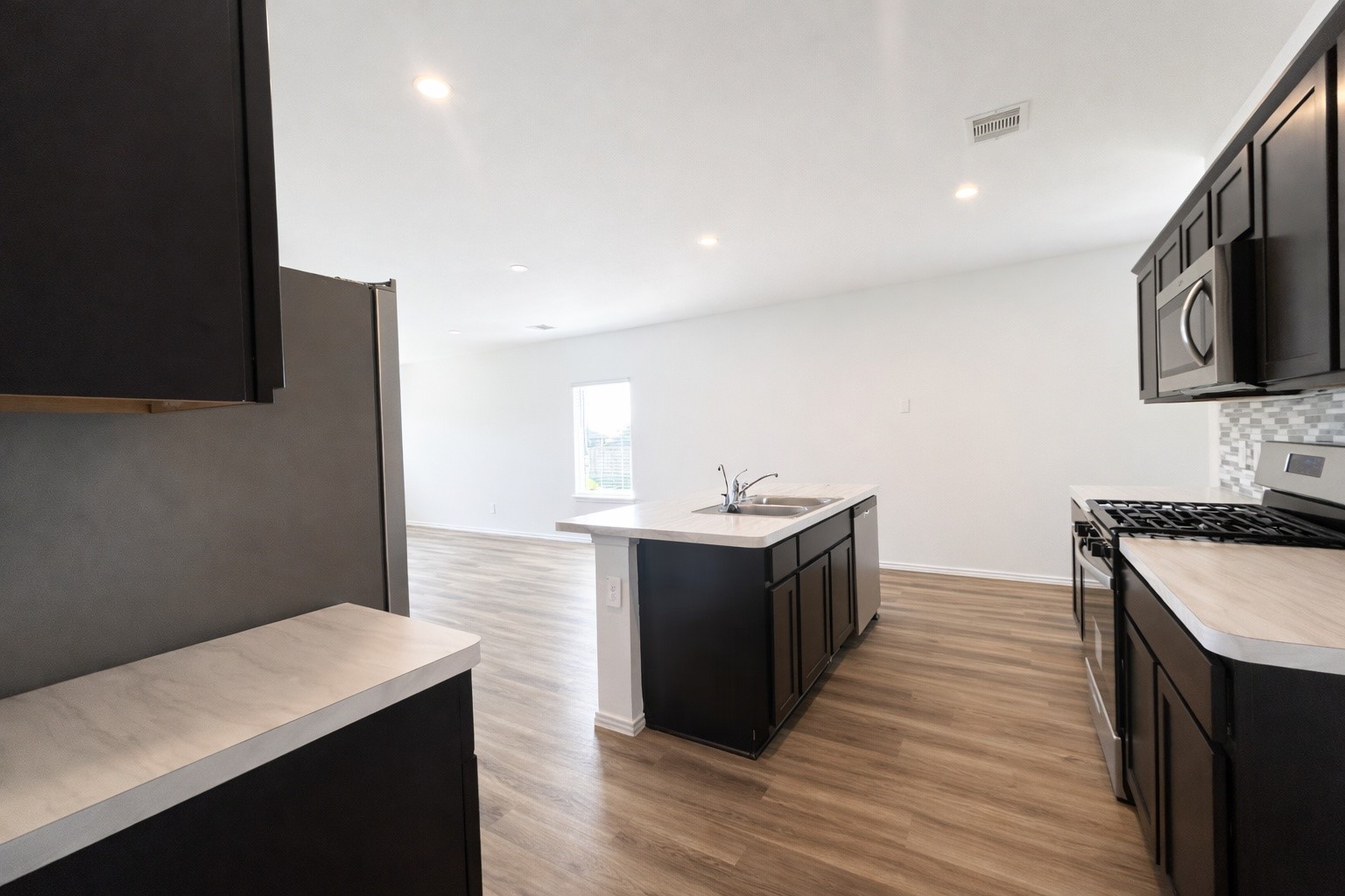 1739 Royal Rim Drive Houston, TX 77014 - Photo 8 of 20 This modern kitchen has dark cabinetry, light countertops, and a stainless steel stove. The space is open and airy, with hardwood floors and an island sink that overlooks a bright living area.