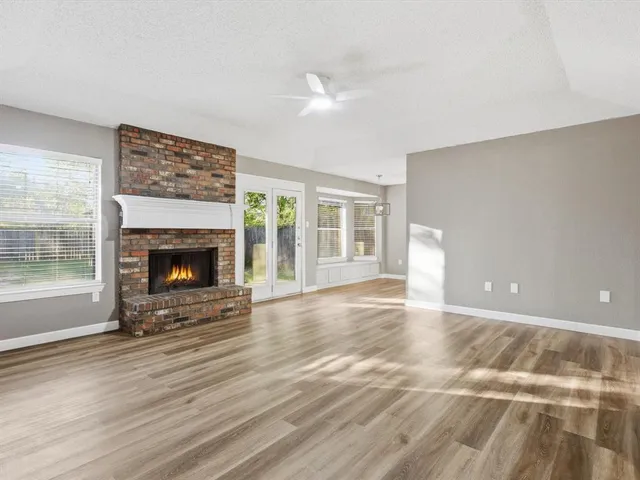a view of an empty room with wooden floor fireplace and a window