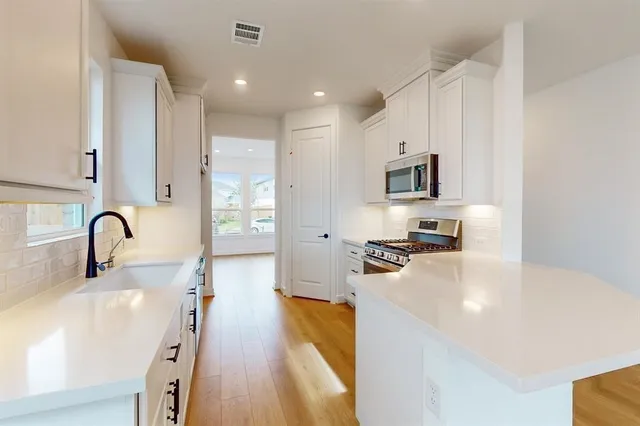a kitchen with stainless steel appliances a stove a sink a refrigerator white cabinets and wooden floor