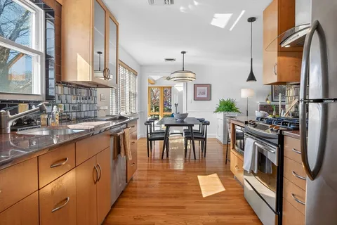 a kitchen with stainless steel appliances granite countertop a stove top oven a sink a dining table and chairs with wooden floor