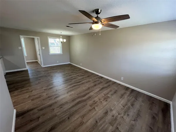 an empty room with wooden floor fan and windows