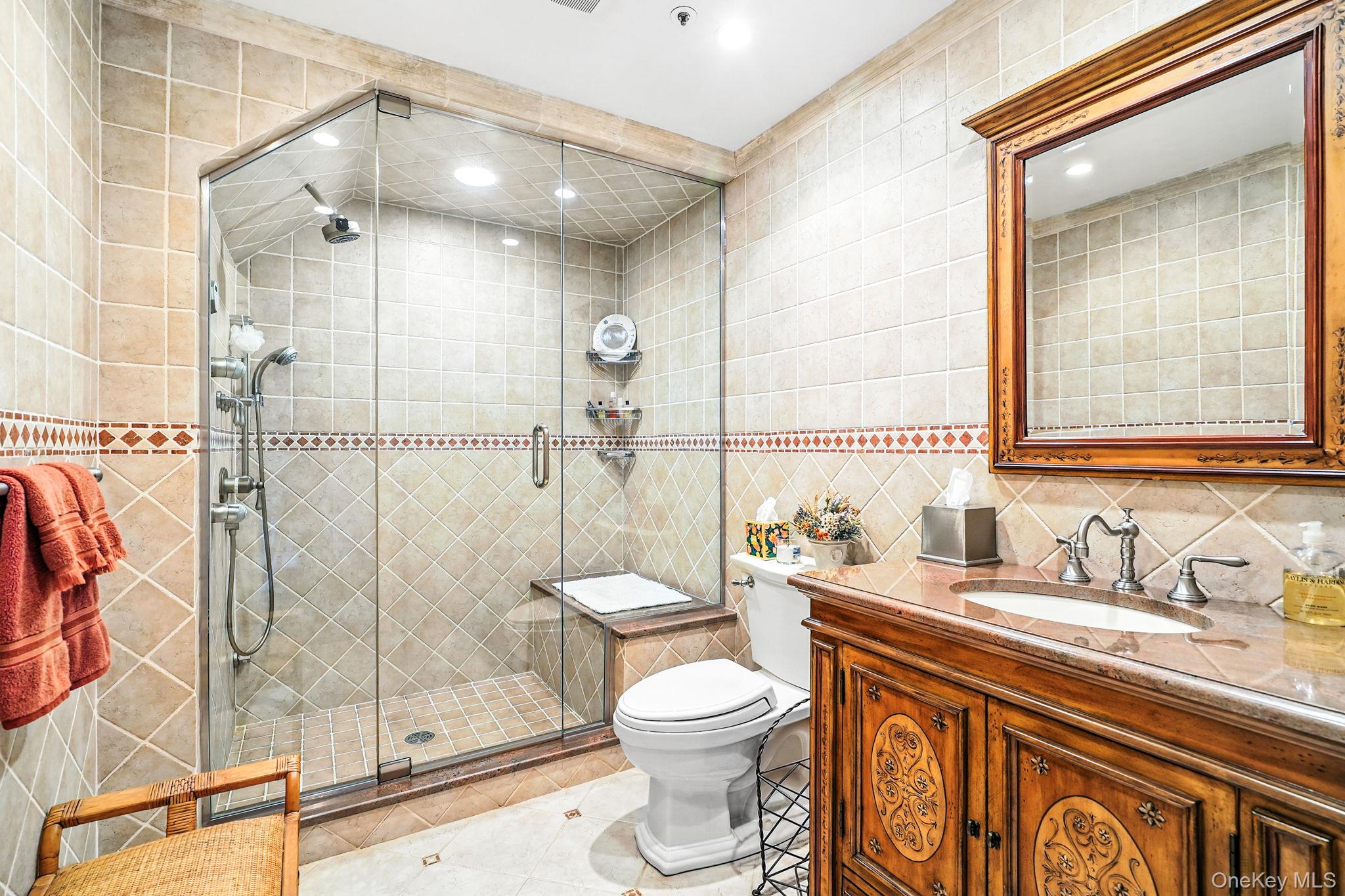 33 Hevelyne Road Elmsford, NY 10523 - Photo 33 of 43 Bathroom in terrace level, featuring tile walls, a shower stall, vanity, light tile patterned floors, and backsplash